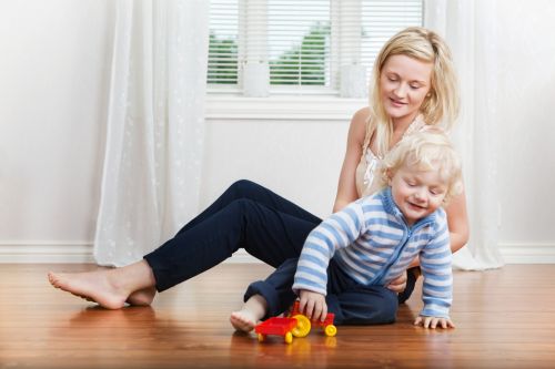Smiling young mother sitting with child playing on floor