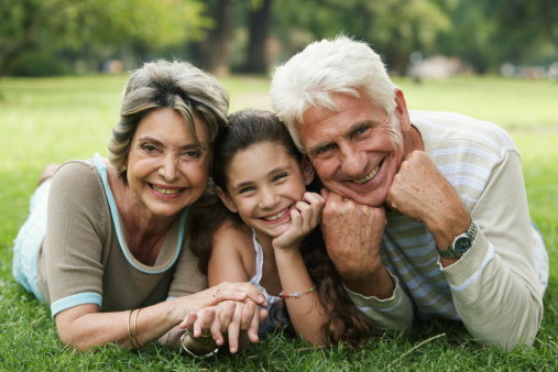 Grandparents and granddaughter (8-10) lying on grass, smiling